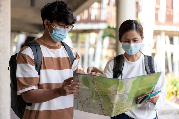 Travel, man and woman are reading paper map. wearing mask, carry backpacks. stripped shirt and eyeglasses.