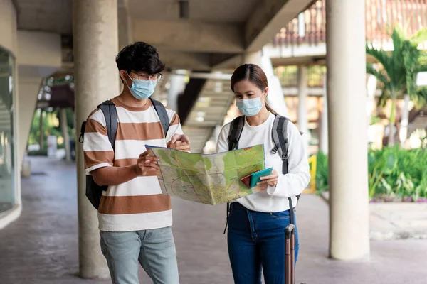 Travel, man and woman are reading paper map. wearing mask, carry backpacks and luggage . stripped shirt and eyeglasses.