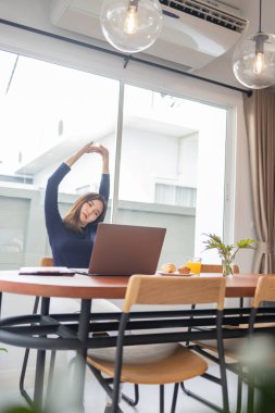 Ev konseptiyle çalışan bir bayan girişimci evinde uzaktan çalışırken kollarını açıp rahatlıyor..