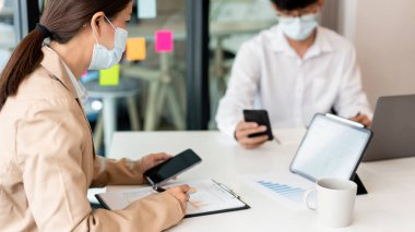 Ameliyat maskesi takan iki meslektaş, pazarlama araştırması için verileri analiz ediyor..