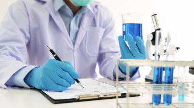 Genç Asyalı bilim adamı mikroskopla inceleyerek adli tıp laboratuarındaki bir deney örneğini analiz ediyor.