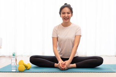 Topuzlu bir kız dikdörtgen yeşil bir mindere oturur ve bacaklarını yere paralel olarak uzatır..