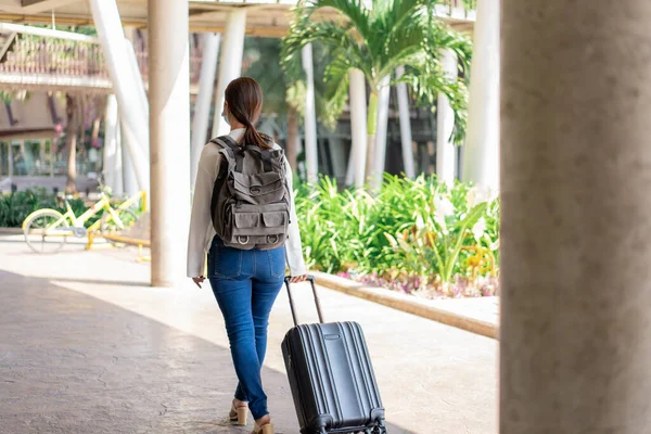 Travel. A woman in a white long-sleeved shirt and jeans, wearing a mask. turn back and walking away with suitcase in the right hand and backpack.