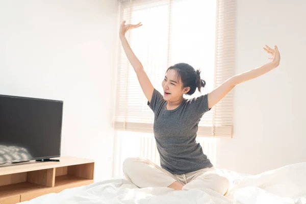 ベッドルームコンセプトA可愛いです女の子見ます眠いですYawning中に彼女の手を伸ばしますザホワイト快適なベッド — ストック写真