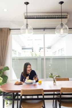 Yemek konseptine sahip genç bir kadın sağlıklı bir yemek yiyor ve cep telefonuyla sosyal medyada vakit geçiriyor..