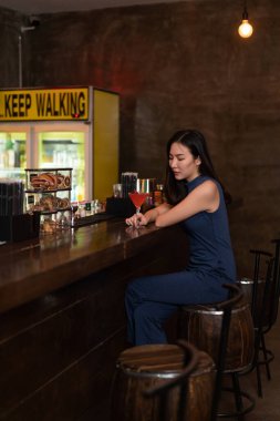 Gece hayatı konsepti. Mavi yakalı, kendine güvenen bir kız. Barın yanında oturmuş pembe kokteyli yudumluyor..