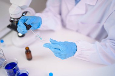 Mavi eldiven giyen profesyonel bilimadamı elleri, mikroskop yakınındaki cam kaydırağında tıbbi araştırmalar yaparak çok önemli laboratuvar deneyleri gerçekleştiriyor.