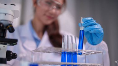 Yetişkin Asyalı kadın bilim adamı laboratuvarda kimyasal deney yapıyor. O, canlı mavi sıvıyla test tüpünü dikkatlice tutar. Bilimsel yenilik.