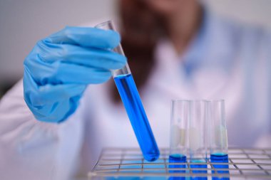 Eldivenli yetişkin bilim adamı, bilimsel deney, tıbbi araştırma ve kimya keşfi için canlı mavi çözeltili cam test tüpü tutuyor.