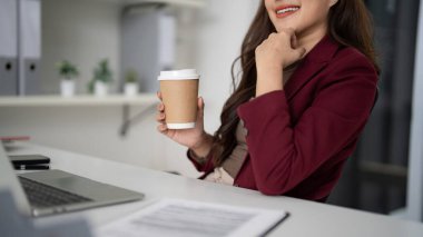 Yetişkin Asyalı profesyonel kahve içer. Ofis işleriyle meşgul. Müşteri yönetimi için dizüstü bilgisayar görünür. Başarılı bir emlakçının günlük odak noktasını yansıtıyor.