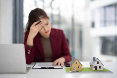 Asyalı yetişkin emlakçı ev modelleriyle çağdaş bir ofis ortamında emlak piyasası konularını düşünmekten bunaldı..