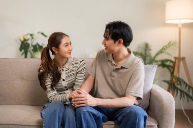 Neşeli Asyalı yetişkinler parlak dairedeki koltukta şefkatli bir bağ paylaşıyorlar. Rahatlatıcı ev atmosferi huzurlu bir mutluluk anı yaratır..