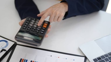 Masanın üzerinde hesap makinesini çalıştıran yaşlı ellere yakın çekim. Profesyonel, finansal verileri analiz eder. İş raporları hazır. Stratejik planlama ve zenginlik yönetimi.