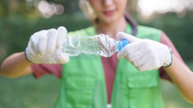 Koruyucu eldiven takan yetişkin Asyalı eller plastik şişeyi atık ayıklamak için eziyor. Çevre bilinci ve çevre temizliği projesinin tanıtımı.