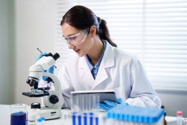 Bilimsel gelişim için laboratuvar ortamında mikroskop ve dijital tabletle dikkatli biyolojik araştırmalar yapan Asyalı bilim adamı.