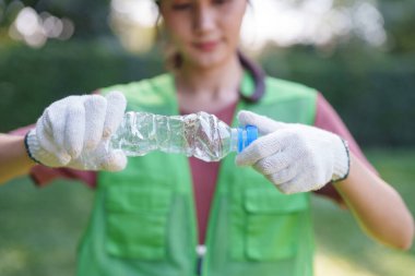 Asyalı yetişkin kadın gönüllü eller plastik şişeyi ezer. Parkın korunmasına yardımcı olur. Ekoloji için atıkların azaltılmasına yardımcı olur.
