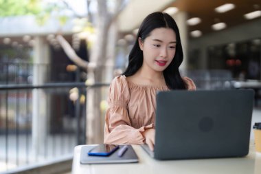 Genç Asyalı kadın, dijital verimliliğin ve modern bağlantının tadını çıkaran bir kafede dizüstü bilgisayarda çalışıyor.