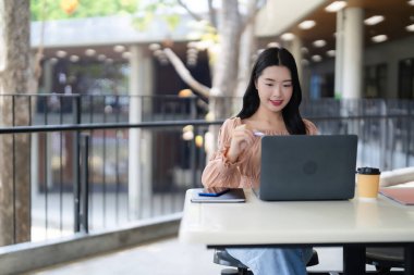 Gülümseyen Asyalı kadın dışarıda dizüstü bilgisayarında stilus kalemle çalışıyor. Uzaktan profesyonel, yaratıcı dijital görevlere odaklanmış. Modern çalışma alanının tadını çıkarıyorum.