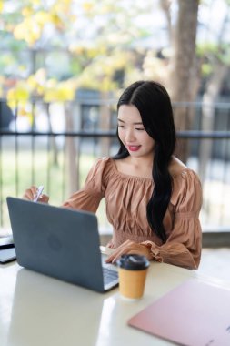 Gülümseyen Asyalı kadın bilgisayarlı stililus kalem kafede çalışıyor ve modern yaşam tarzının tadını çıkarıyor.
