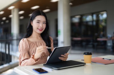 Gülümseyen Asyalı kadın dijital ped stili ile meşgul yaratıcı proje günlük ayarlama odaklı öğrenci iş veya eğitim teknolojisi kullanarak.