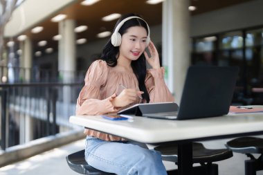 Genç Asyalı kadın bilgisayar tabletinde çalışırken kulaklık dinliyor. Sanal sınıf uzaktan kumandanın keyfini çıkarıyor. Verimliliği yoğunlaştırıyor.