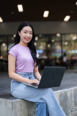 Genç Asyalı kadın dışarıda dizüstü bilgisayar kullanıyor. Çevrimiçi uzaktan çalışma dijital verimliliği öğrenen mutlu kadın.