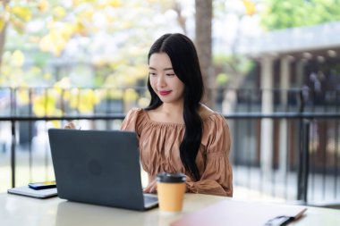 Asyalı yetişkin kadın dışarıda dizüstü bilgisayarda özenle çalışıyor. Üretkenliği arttırmak için stil kullanıyor. Sıradan iş ortamı.