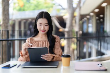 Genç Asyalı kadın yaratıcı proje dijital tablet stili üzerinde çalışıyor açık kafede üretken uzaktan çalışma ya da öğrenim