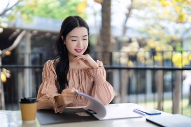 Genç Asyalı bayan dışarıda iş evraklarını inceliyor. Taze havanın tadını çıkararak strateji planlaması raporlarına odaklanıyor..