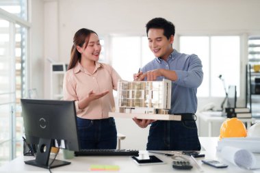 Profesyonel Asyalı mimarlar, başarılı takım çalışmalarını, yenilikçi tasarım planlamasını ve mülkiyet gelişimini gösteren parlak ofis ortamında yapı modelini birlikte analiz ederler.