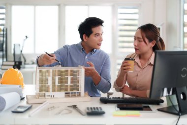 Yetişkin Asyalı mimarlar ofislerinde bir yapı modeli tasarımı üzerinde işbirliği yaparak yenilikçi proje planlarını tartışıyor takım çalışması beyin fırtınası yapıyor profesyonel işyeri çözümleri belirliyor