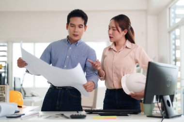 Profesyonel Asyalı mühendisler, çağdaş bir ofis ortamında proje geliştirmeyi tartışan mimari planların gözden geçirilmesinde işbirliği yapıyorlar.