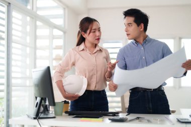 Yetişkin Asyalı profesyoneller mimari planları analiz ederler. Ekip çalışması planlama projesiyle uğraşıyorlar. Modern ofis ortamı işbirliğini teşvik ediyor