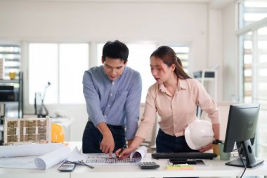 Profesyonel Asyalı mimari mühendislik ekibi özenle ofis işyeri inşa tasarımı ile işbirliği yaparak mimari planlar ve gelecek geliştirme projelerini gözden geçirir..