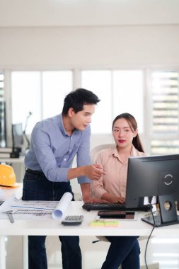 Asyalı yetişkin profesyoneller ofis masasında iş birliği yapıyor. Adam bilgisayar ekranını gösteriyor. Kadın tipleri. Mimari planlar ve tasarım üzerine takım çalışması. Parlak çalışma alanında proje tartışması.