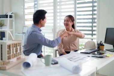 İki gülümseyen Asyalı yetişkin profesyonel ofis masasına yumruk tokuşturarak başarılı takım çalışması projesini tamamlıyor yeni iş ortaklığı başarısını simgeliyor.