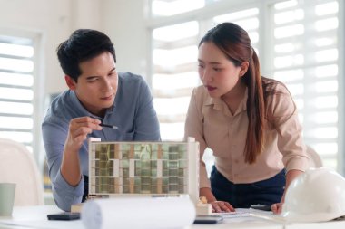 Profesyonel Asyalı mimarlar modern bir ofiste mimari bir modeli incelemek için işbirliği yaparlar. Kentsel planlama ve yaratıcı tasarım çözümlerini tartışıyorlar..