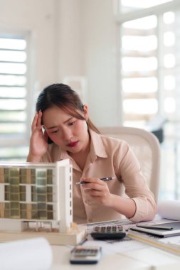 Karmaşık bina modelini inceleyen endişeli kadın mimar. Geliştirmeyi planlıyor, profesyonel çalışma alanında tasarım zorluklarının üstesinden geliyor..