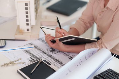 Mimari planlar ve tasarım planları üzerinde titizlikle çalışan yetişkin bir mimar profesyonel ofis ortamında kalemle notlar alıyor.