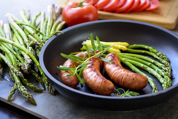 Salsicce fritte con asparagi, pomodori e rosmarino su una padella — Foto Stock