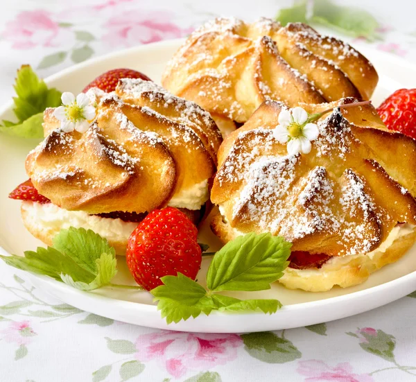 Bouffées de crème ou profiterole garnies de crème fouettée, garniture de sucre en poudre servie avec des fraises sur la table — Photo