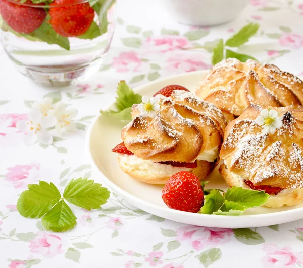 Bocadillos de nata o profiterole rellenos de nata batida, relleno de azúcar en polvo servido con fresas sobre la mesa — Foto de Stock