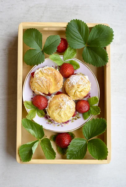 Bouffées de crème maison ou profiterole rempli de crème fouettée, garniture de sucre en poudre servie avec des fraises dans un plateau en bois — Photo