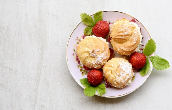 Puffs de creme ou profiterole preenchido com chantilly, cobertura de açúcar em pó servido com morangos em uma placa cinza pedra — Fotografia de Stock