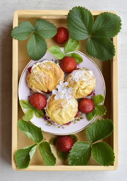 Cream puffs or profiterole filled with whipped cream, powdered sugar topping served with strawberries in a wooden tray — Stock Photo, Image