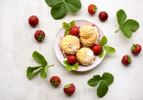 Cream puffs or profiterole filled with whipped cream, powdered sugar topping served with strawberries on a stone grey board — Stock Photo, Image