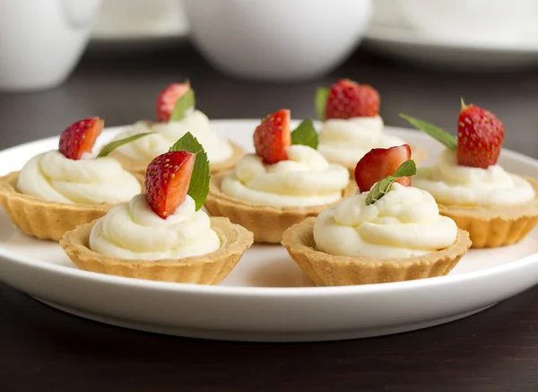 Viele Kuchen, Cupcakes mit frischen Früchten (Erdbeeren), Schlagsahne und Minzen — Stockfoto