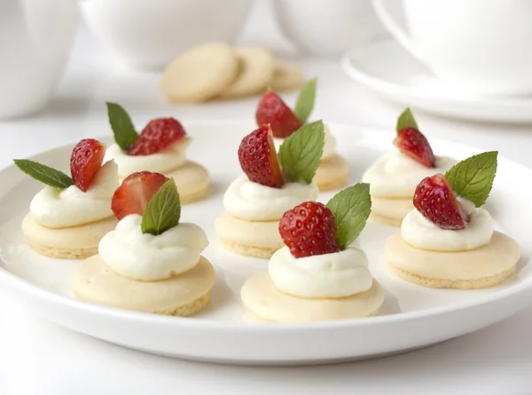 Small biscuits with whipped cream, strawberry, mint on white plate on table against light background — Stock Photo, Image