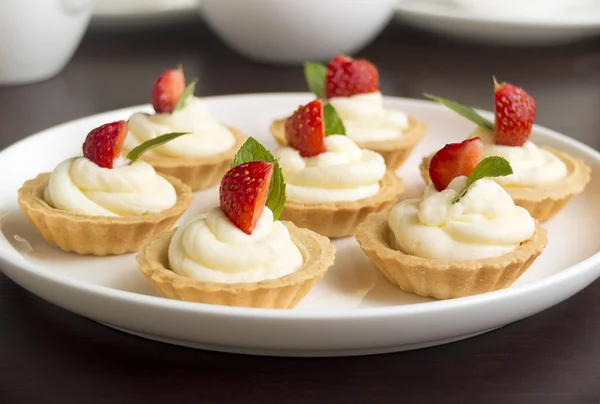 Small biscuits with whipped cream, strawberry, mint on white plate on table — Stock Photo, Image