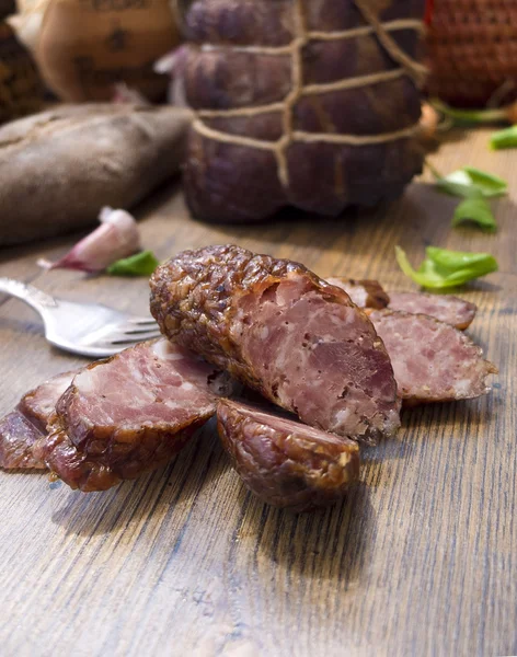 Slices of sausages and gammon ham with bread, tomatos, herbs, garlic and basketson wooden board — Stock Photo, Image